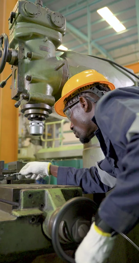 African technician bends beside drill press in vertical frame, inspecting work Stock Footage 341398877