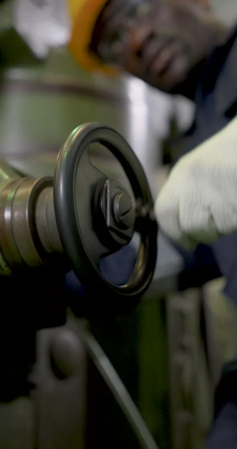 African technician turns machine handwheel in vertical frame, adjusting drill Stock Footage 339049628