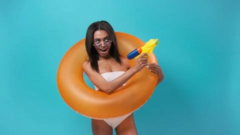 African woman dancing with an inflatable circle in a swimsuit with a water gun Stock Footage 200212955