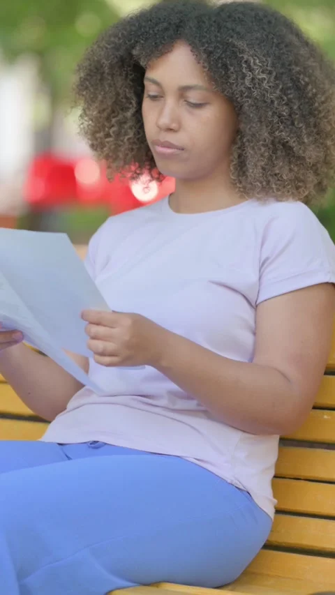 African Woman Reading Documents while Sitting Outdoor, vertical Видео 326264654