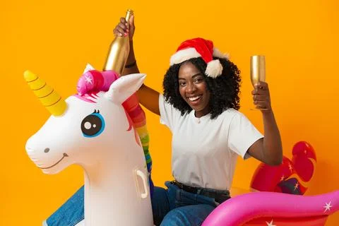 African woman sitting on rainbow unicorn float wearing santa claus hat in studio Stock Photos