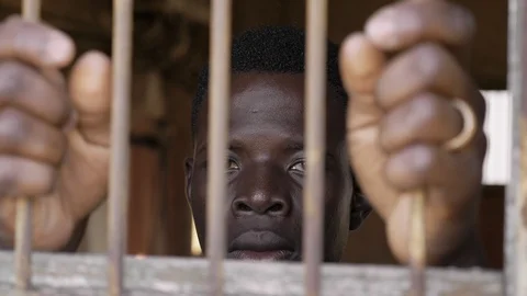 African young man behind bars staring at camera. Illegal migration,human rights Stock Footage