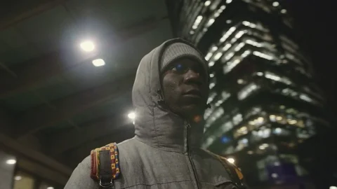 African young man in a jacket looks around at night. He looks forward. He has a Stock Footage 102437515
