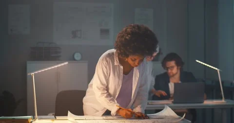 Afro-american architect working in office with blueprint late in evening Stock Footage 154148208