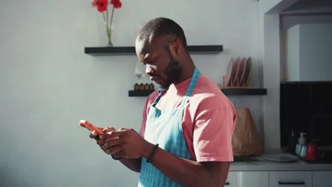 Afro-american attractive man using browsing on Internet while cooking. Cheerful Stock Footage 131669300
