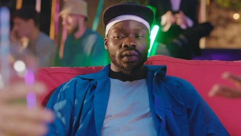 Afro-american cool guy with bored expression relaxing on coach with friends Stock Footage 115354453