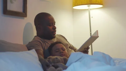 Afro-American Dad Reading Book to Sleeping Kid in Bedroom Stock Footage 136216024