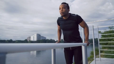 Afro american guy workout on dips bars near the city lake Stock Footage 121321289