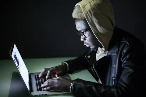 Afro american Hacker in Hood using Laptop Computer in the Dark hack networks  Stock Photos