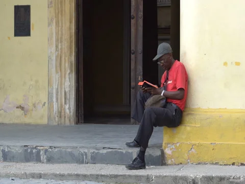 Afro-American man dressed red t-shirt, trousers, glasses sits at the corner of Stock Footage 69559154
