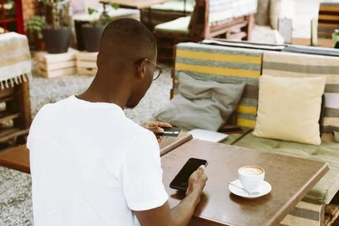 Afro american man sitting at table in cafe with cup of coffee on summer veranda Stock Photos