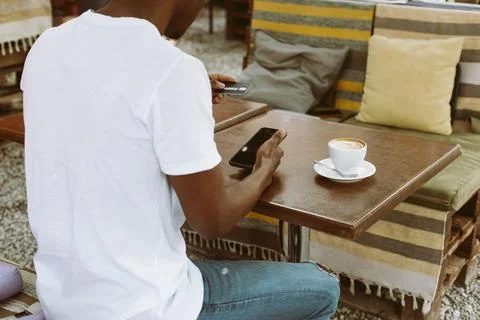 Afro american man sitting at table in cafe with cup of coffee on summer veranda Stock Photos