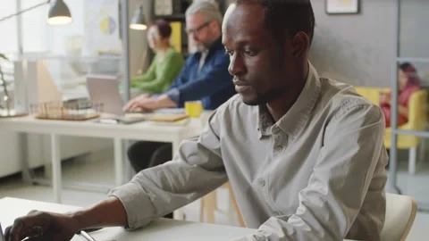 Afro-American Man Using Laptop and Reading Document at Work in Office Stock Footage 156441422