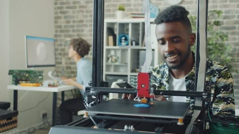 Afro-American man using tablet looking at 3d printer manufacting model in office Stock Footage 119557408