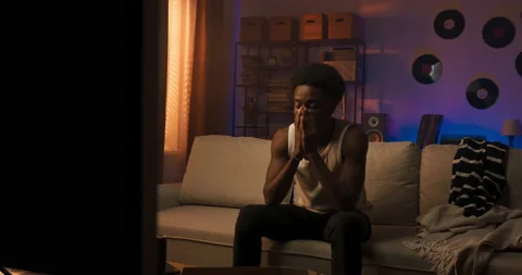 Afro athletic man sits on the couch wearing a white T-shirt with straps, the guy Stock Footage 200417620