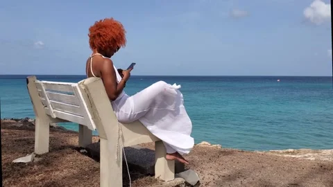 Afro Latina woman using smartphone sitting on bench in the Caribbean Stock Footage