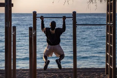 Afro man doing pull ups on horizontal bar at the beach. Sport And Lifestyle. Photos