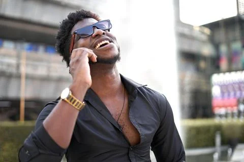 Afro man laughing while talking to the mobile outdoors Stock Photos