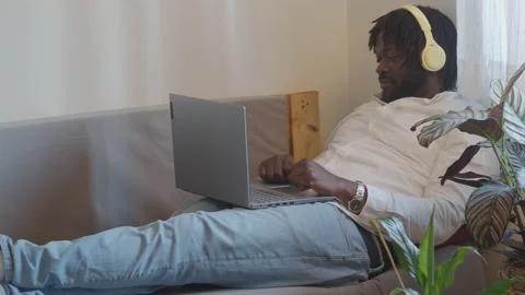 Afro man making a video call with a laptop from on a sofa at home Stock Footage 147547908
