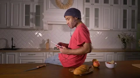Afro man in modern kitchen sitting on kitchen table, using smart phone and Stock Footage 167703125