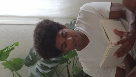 Afro man reading a book sitting on the floor in a apartment. Vertical video Stock Footage 159449897