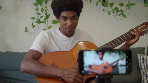 Afro man recording himself with the mobile while playing the guitar. Stock Footage 159725924