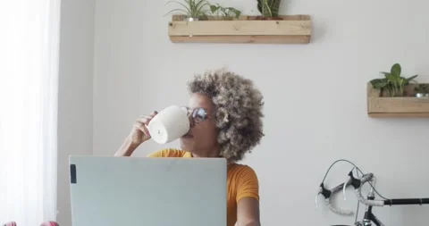 Afro woman drinking coffee while working at home or in an office with a laptop Stock Footage 161673998