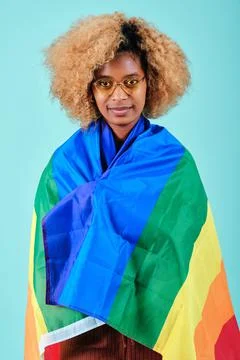 Afro woman looking into camera while wrapped with a pride flag over an isolated Stock Photos