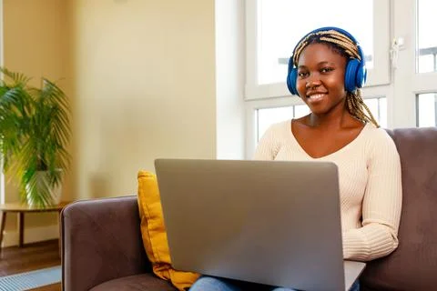 Afro woman working by laptop and listening audio lesson in living room at home Stock Photos