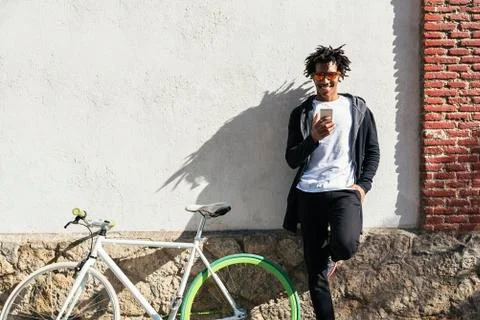 Afro young man using mobile phone and fixed gear bicycle. Stock Photos