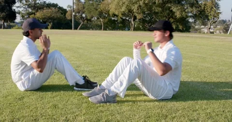 After adjusting baseball caps diverse male friends performing sit-ups on grass Stock Footage 340009209