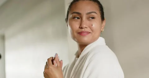 After applying hand cream, mid 30s Asian woman rubbing hands at vanity for calm, Stock Footage 342718634