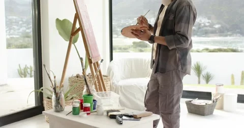 After assessing canvas, male painter is dipping brush in green paint to create 库存影片 344644802