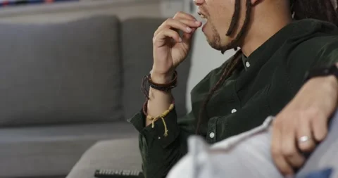 After camera pan, dreadlocked man is picking popcorn from bowl on lap and Stock Footage 336535359