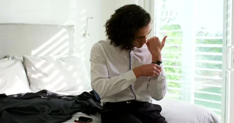 After checking watch African American man sitting on bed adjusting strap and Stock Footage 341027979