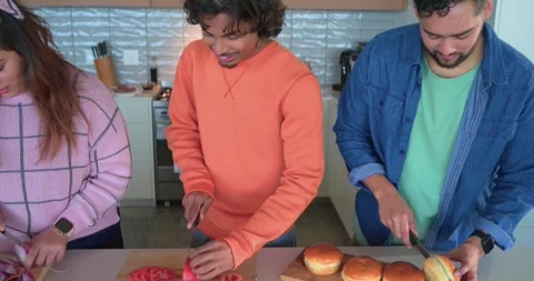 After deciding dinner diverse friends slicing onion, tomato and buns on kitchen Stock Footage 338325730
