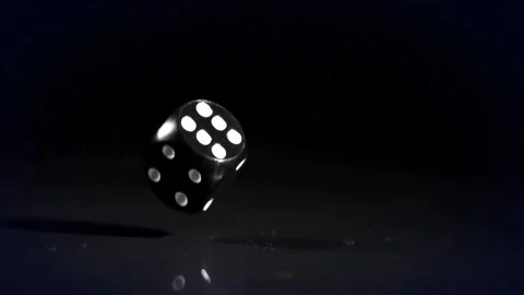 After initial toss glossy black die tumbling and rotating above mirror table 動画素材 328384256