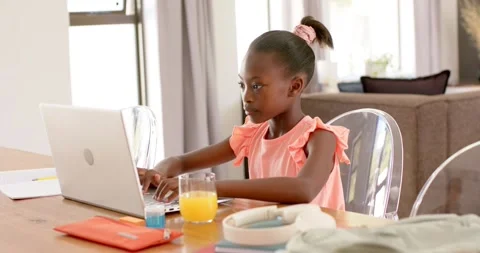 After opening laptop, school aged African American girl sitting at dining table Stock Footage 341736491