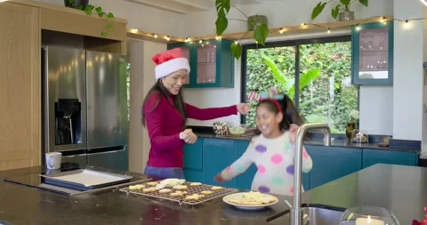 After placing cookies on rack, Diverse mother and daughter dancing at countertop Stock Footage 336658215