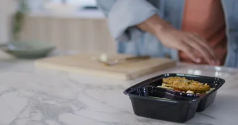 After plating, African American man in denim sealing trays with clear lids at Stock Footage 337239313