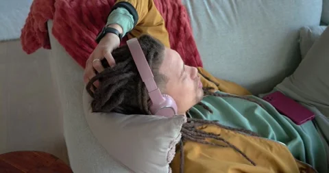 After scrolling smartphone man reclining on couch at home adjusting headphones Stock Footage 344383269