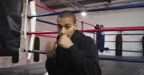 After stepping into boxing ring, male boxer wearing hoodie punching and grabbing Stock Footage 340009273
