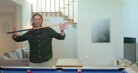 After striking ball on blue-felt pool table, man at home pumping stick Stock Footage 344946742