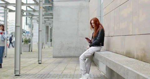 After walker passing, woman scrolling phone at plaza bench shifting and smiling, Stockbeeldmateriaal 344330748