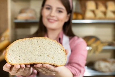 Against the backdrop of the bread shelves, a young attractive saleswoman shows a 写真素材
