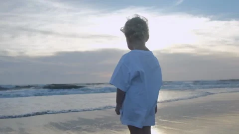 Against the backdrop of a sea sunset, a three-year-old child in a long T-shirt Stock Footage 214673030
