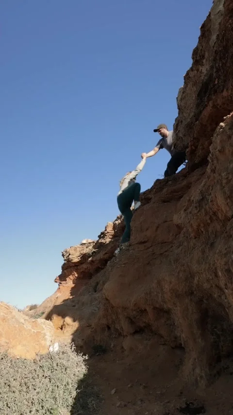 Against the backdrop sky, a man extends his hand to help a woman climb the .. Vídeo Stock 267466469