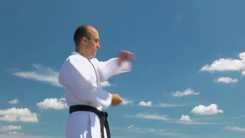 Against the background of a blue sky with clouds, an athlete trains punches Stock Footage 141281883