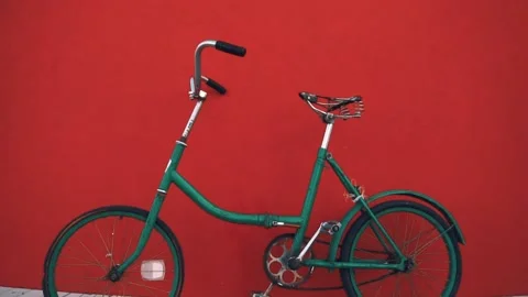 Against the background of a red wall, an old rusty green bicycle with flat tires Stock Footage 147405821