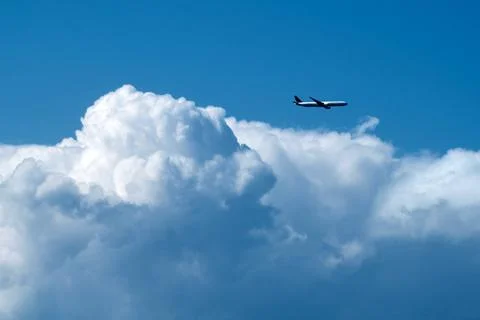 Against the blue backdrop, a massive, formless cloud floated while a plane .. Stock Photos